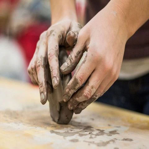 Hands shaping wet clay on a wooden table, symbolizing mindfulness through clay art.