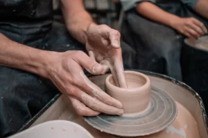 Close-up of hands shaping a clay pot on a pottery wheel, with wet clay and fingers gently molding the vessel in a studio setting.